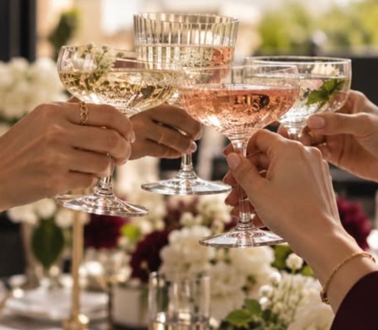 Des mains trinquent avec des coupes de champagne au-dessus de fleurs blanches et bordeaux